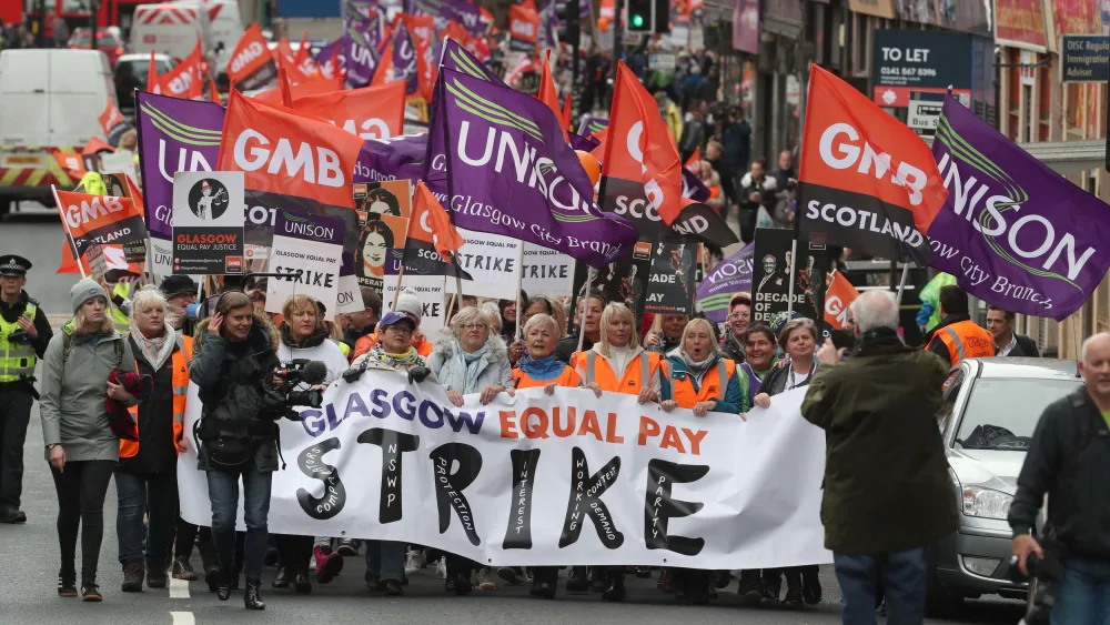 A large number of people taking part in a march, holding GMB and Unison flags and placards