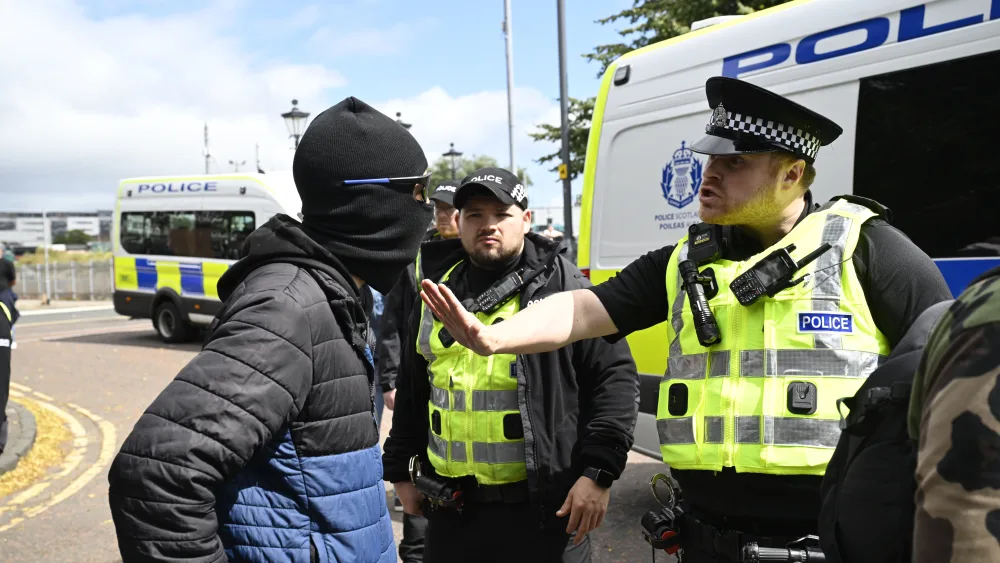 A police officer taking to a protester who is wearing a black balaclava