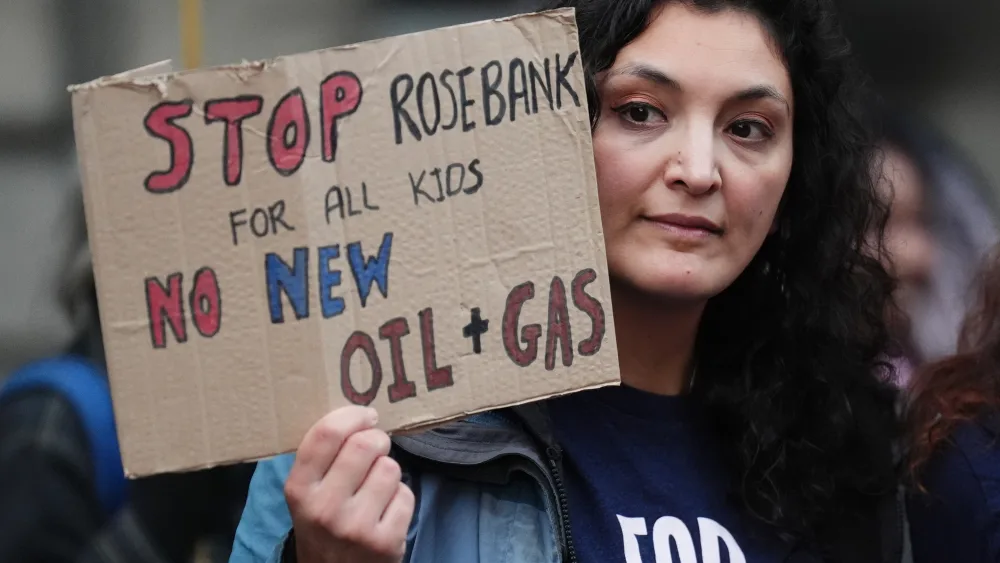 A woman holding a sign reading 'Stop Rosebank for all kids. No new oil and gas'