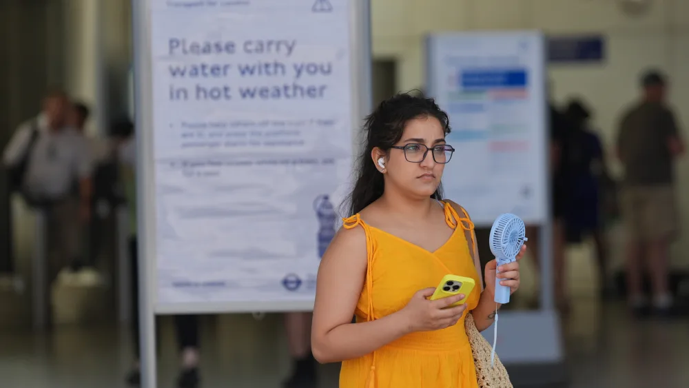 A woman using a handheld electric fan while walking outside a London station 