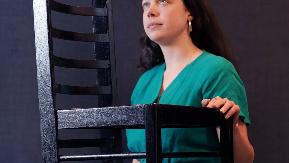 A woman standing beside a Charles Rennie Mackintosh-designed ladderback chair