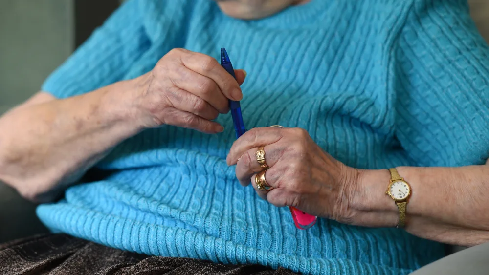 An elderly lady holds a pen