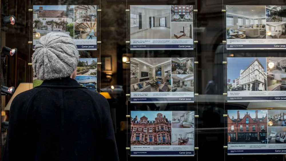 A woman looks at houses for sale in the window of an estate agents