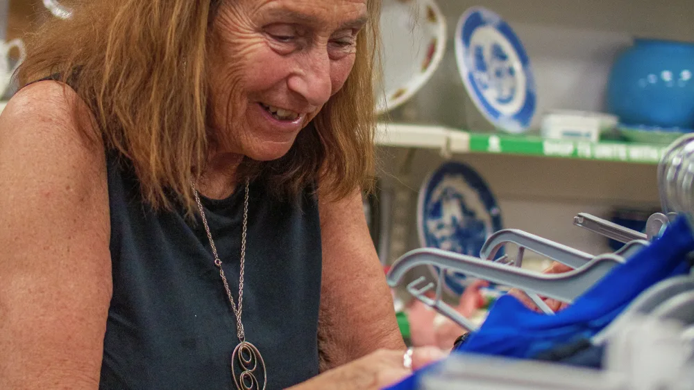 Barbara Myloff smiling while sorting clothes on hangers in a shop