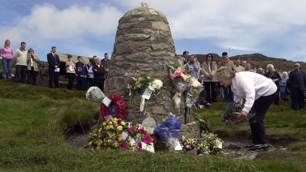 A woman lays flowers at the foot of a memorial cairn