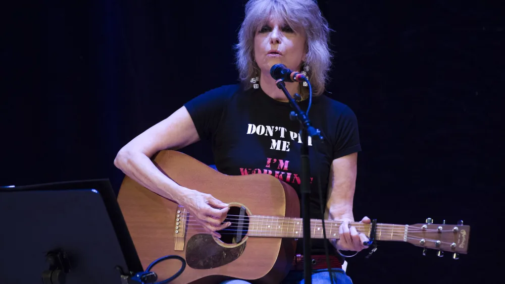 Chrissie Hynde sitting down playing a guitar in front of a microphone