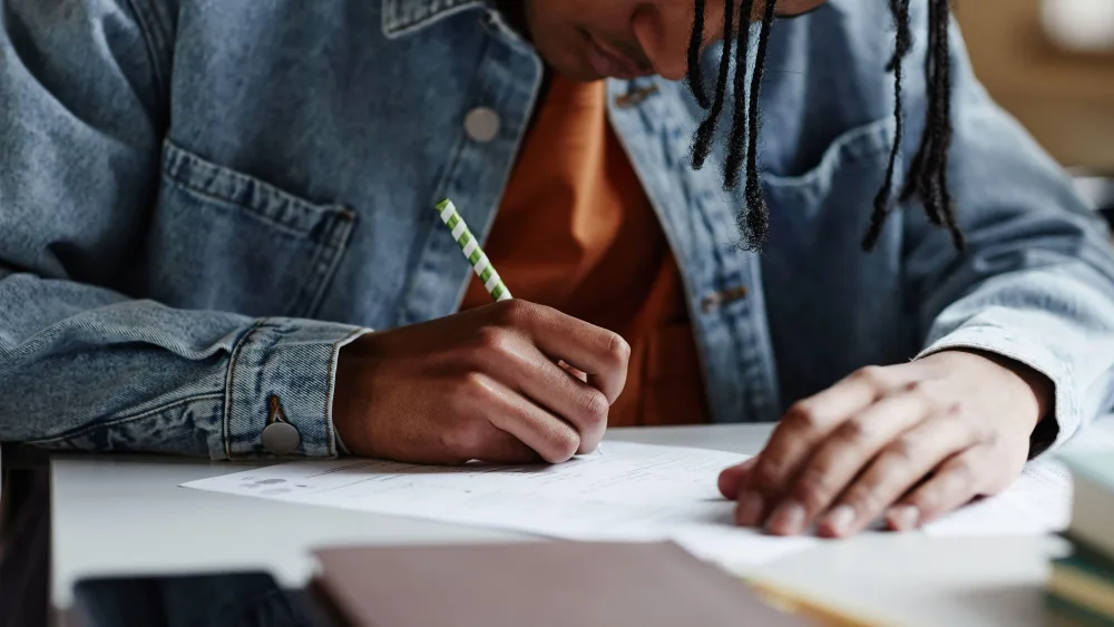 A student writing on paper at t desk