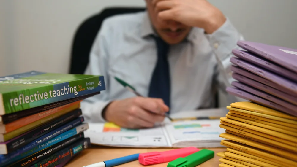 A stressed teacher marks a pile of jotters