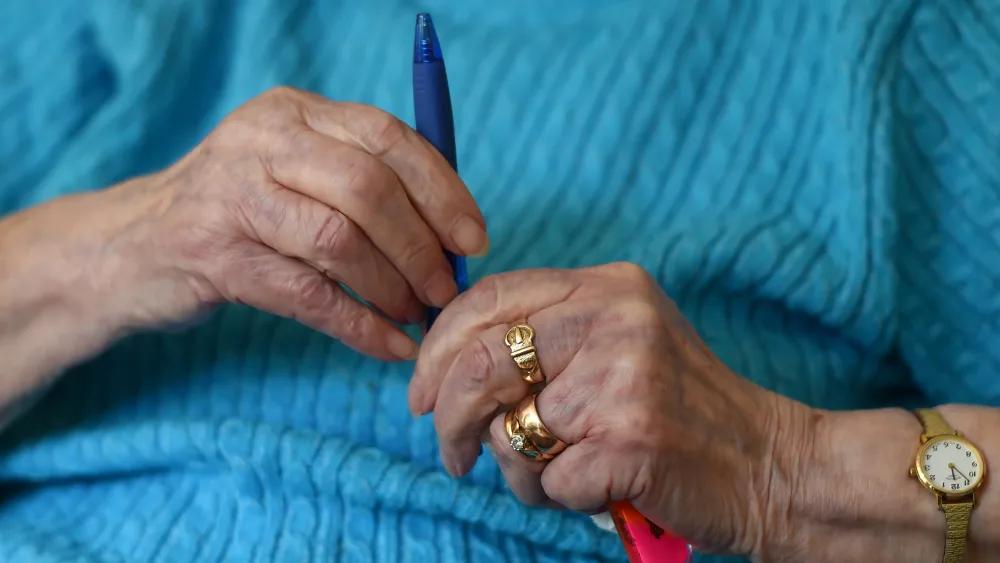 An elderly woman holds a pen