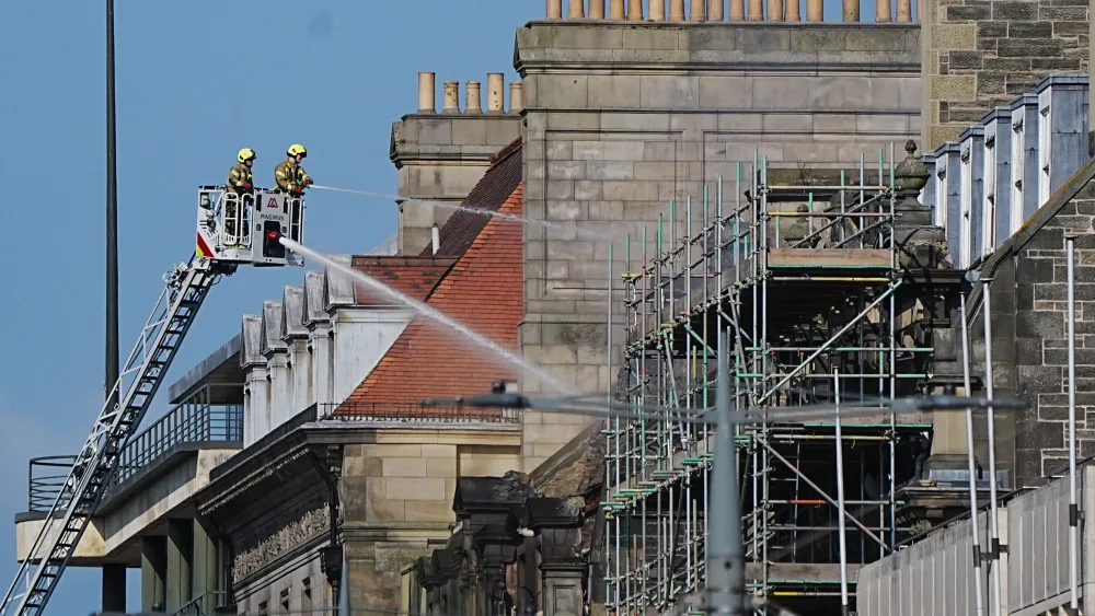 Firefighters on a high platform aim a hose at a building, which is showing signs of fire damage