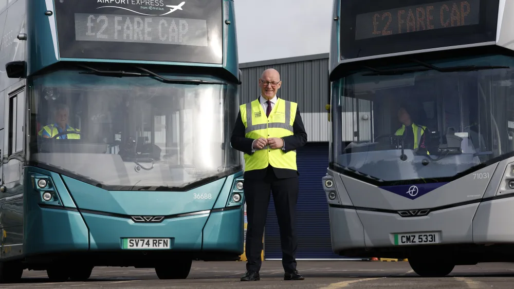  First Minister John Swinney stands in front of two buses