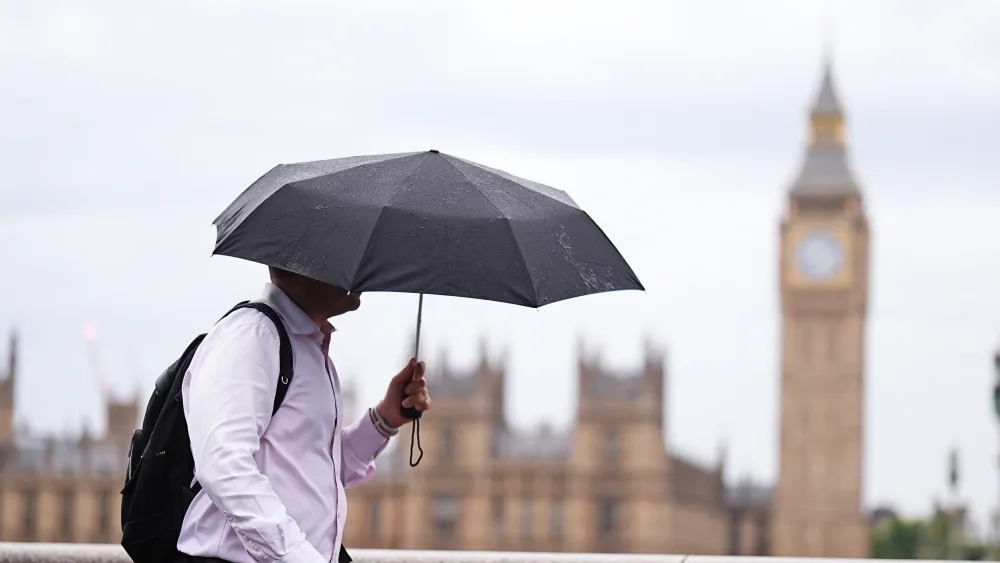 A person uses an umbrella while out walking, with the Houses of Parliament in the background