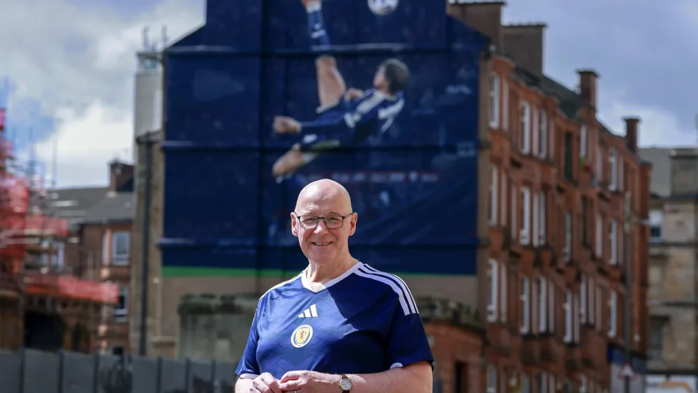 John Swinney standing in front of a mural showing Scott McTominay's overhead kick
