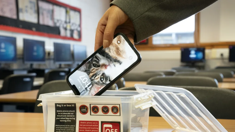A pupil puts a mobile phone into a holding box in a classroom