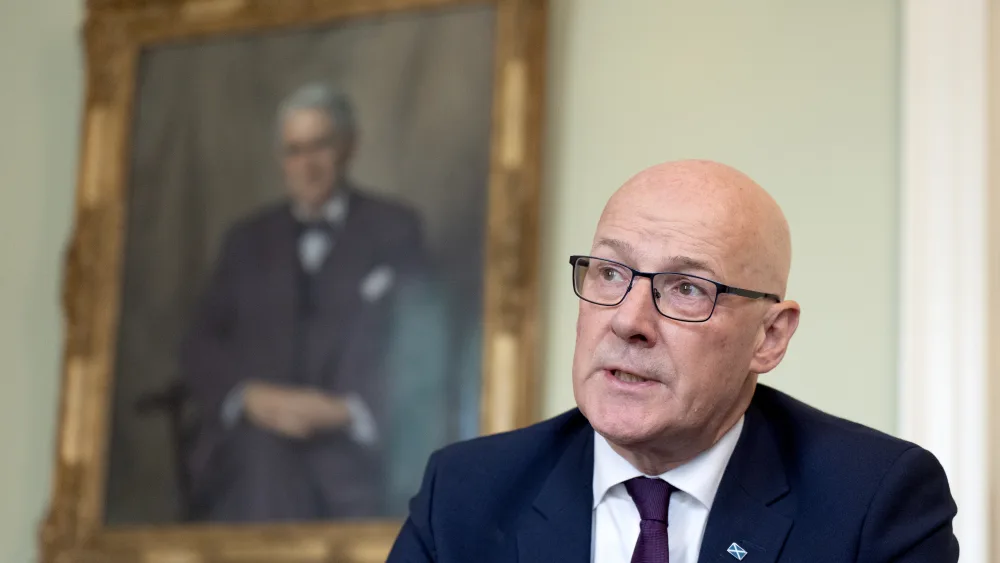 John Swinney speaking, with a portrait hanging on the wall behind him