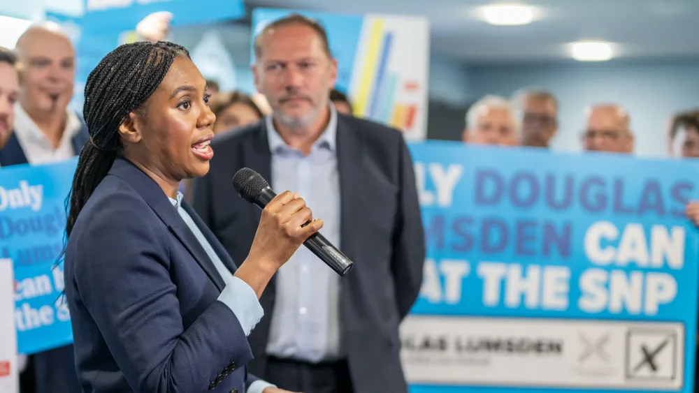 Kemi Badenoch speaking into a mic, as Douglas Lumsden looks on, in front of Tory supporters