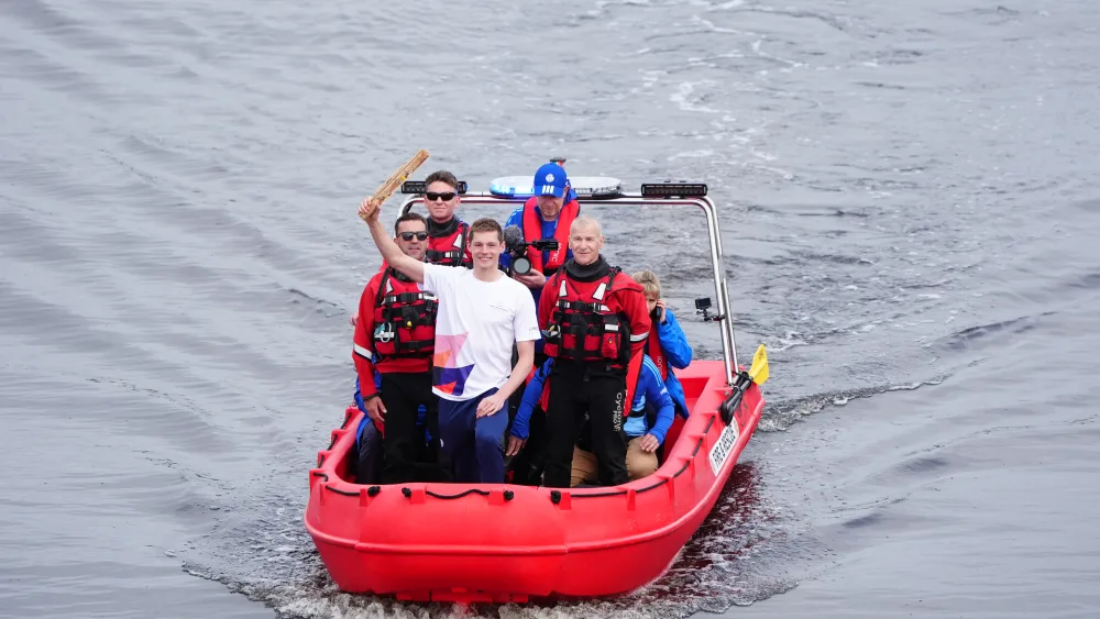 Duncan Scott holding the King's Baton aloft and smiling while on a boat on a river