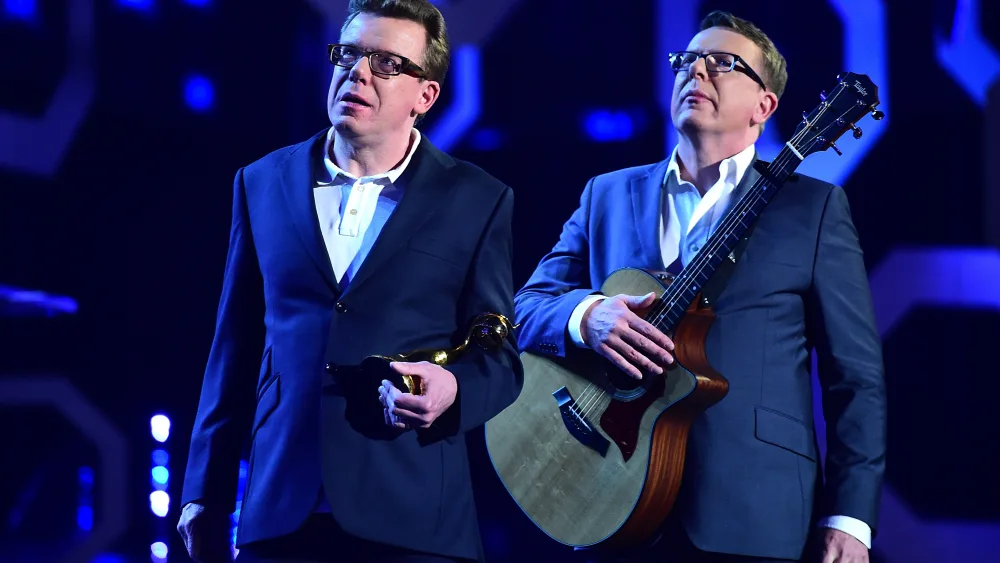 The Proclaimers standing on stage, one holding a guitar and the other holding an award