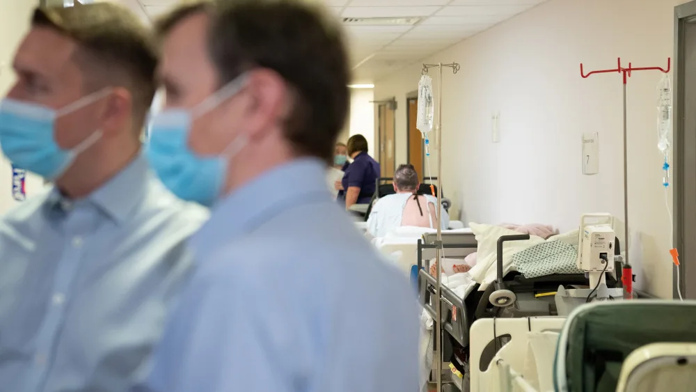 Patients wait on beds in a hospital corridor