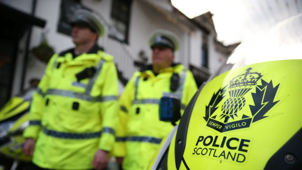 Police Scotland officers in uniform, walking past a police motorbike