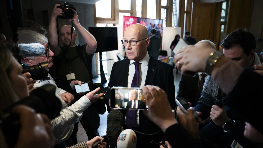 John Swinney speaking while surrounded by members of the press