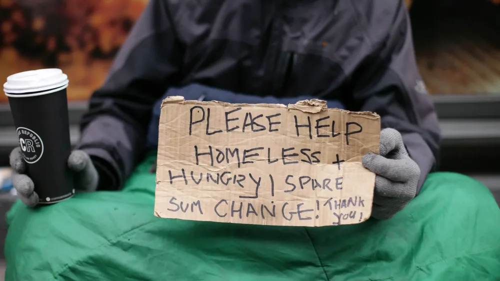 A homeless person sitting on the ground holding a sign asking for spare change