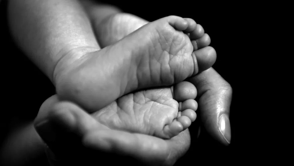 A black and white photo of a baby's feet in an adult's hand