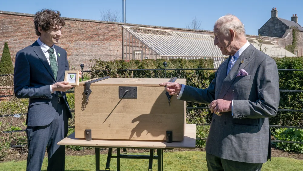 The King being presented with a boxed Blue Peter Green Badge by Joel Mawhinney, in a garden