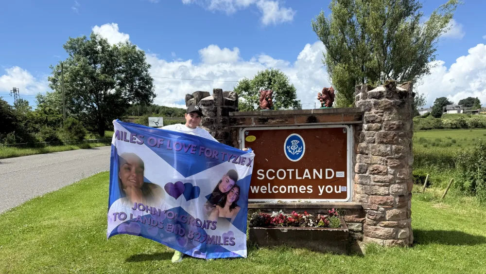 Caitlin Andrew with a Saltire next to a Scotland welcomes you sign