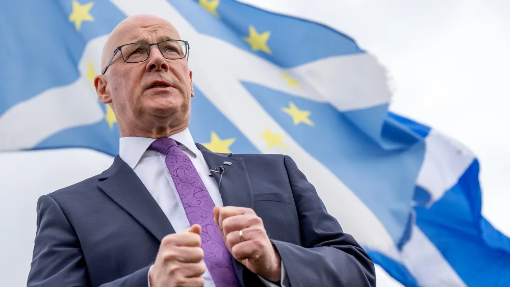 John Swinney speaking in front of Scottish flags