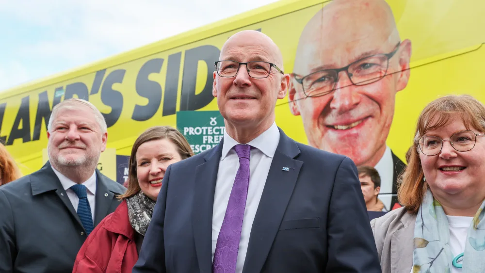 John Swinney smiling alongside SNP supporters in front of the SNP battle bus