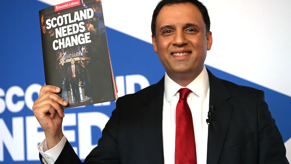 Anas Sarwar smiling while holding up a copy of the Scottish Labour manifesto