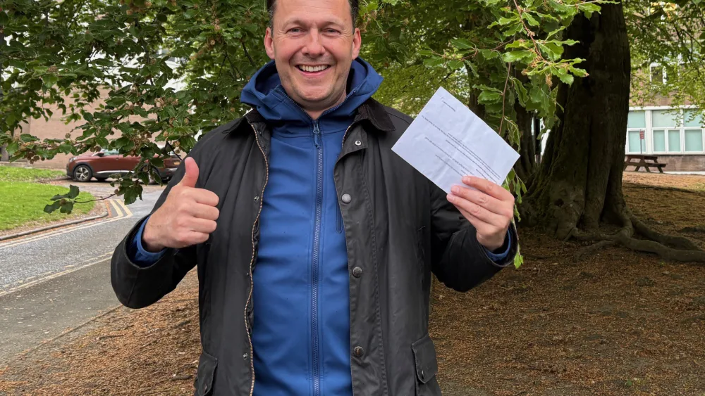 Russell Findlay smiling and giving the thumbs up, while holding his polling card