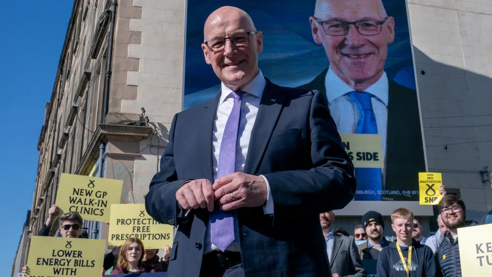 John Swinney smiling in front of a large photo of himself on the side of a building