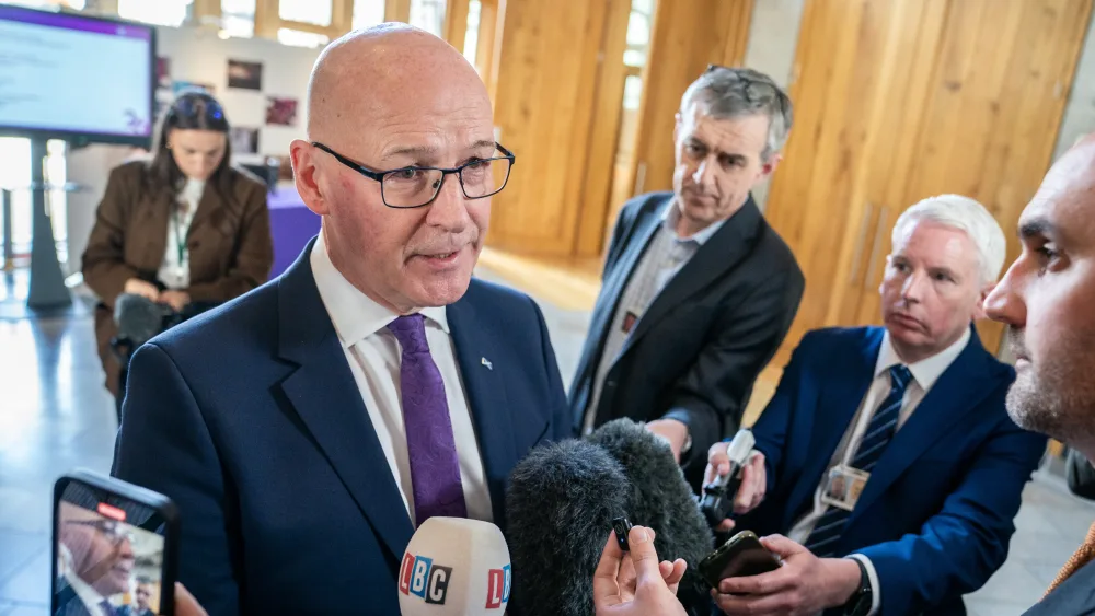 John Swinney in front of a loaf of microphones talking to the media