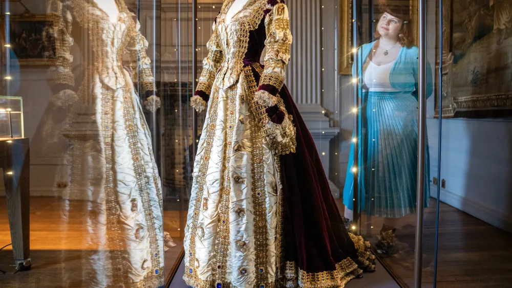 A Mary, Queen of Scots costume on display in a cabinet, with a woman looking at it