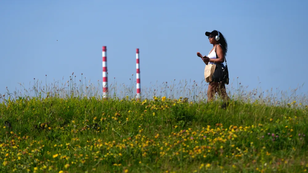 A woman walks on a grassy hill in the sunshine, beneath clear clue skies