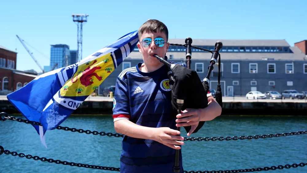 A man playing the bagpipes while wearing a Scotland top