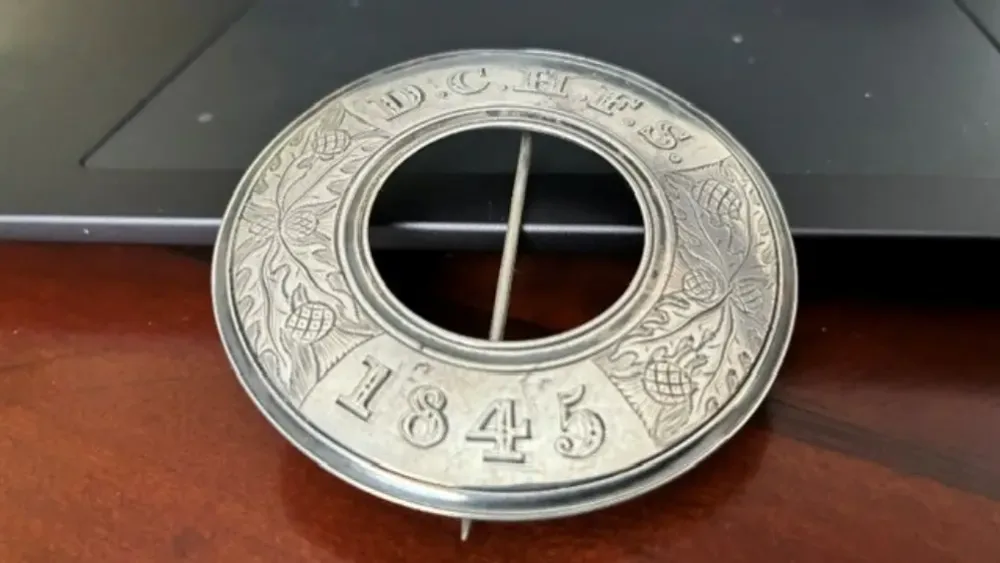 View of a silver brooch, which has the middle cut out, with an inscription round the edge