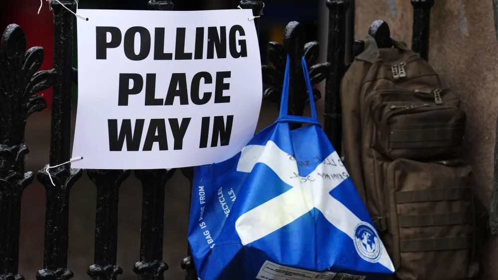 A polling place sign on a fence, with a bag featuring the Scottish saltire hanging beside it