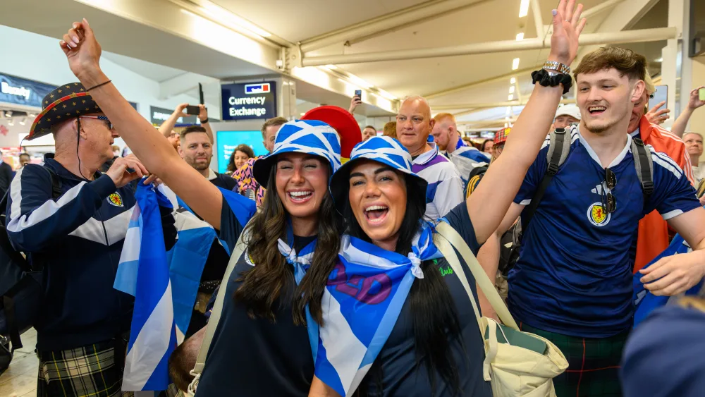 Women wearing Scottish hats and flags smiling amid a crowd of Scotland fans