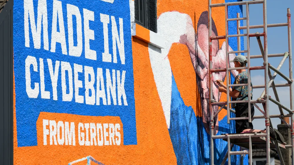 A painter works on a mural of John McGinn on the side of a house